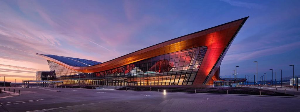 a sleek, modern architectural fa&ccedil;ade of the cardiff international sports village showcases sharp geometric lines, expansive glass surfaces, and the innovative integration of sustainable materials, embodying the principles of functional innovation and aesthetic minimalism under bright artificial lighting.
